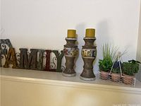 Two wooden carved candlesticks with yellow pillar candles on top, next to a metal FAMILY sign with a rustic finish.