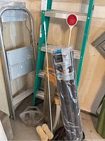 Full view of ladders, saw, brush, safety mirror, jumper cables, and foam insulation packaging in garage corner.