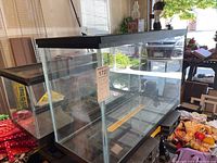 Wide view of two glass aquariums stacked in a garage space. Both have black metal frames and screen tops. Larger aquarium in front, smaller behind.