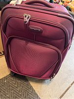 Front view of the maroon Samsonite carry-on roller bag with dual zipper pulls and front zippered pocket
