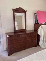Full front view of the nine-drawer mahogany dresser with the separate beveled mirror resting on top but not attached to the wall.