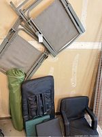 View of two beige folding chairs leaning against the garage wall, green camping chair bag beside them, and two black stadium seats on the ground beneath.