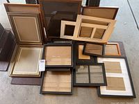 Photo showing assortment of over 16 picture frames in different sizes and colors laid out on ground, some with mats and glass.