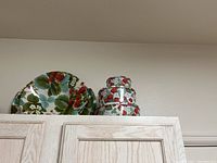 Photo of three strawberry-patterned tins stacked on top of light wood kitchen cabinets alongside two large melamine dishes with matching strawberry design.
