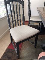 Full side view of one black oak dining chair with spindle back and beige fabric padded seat, showing turned legs and stretchers.