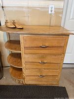 Front view of vintage wooden cabinet with three drawers and three curved shelves. Pair of adjustable wooden shoe trees placed on top.