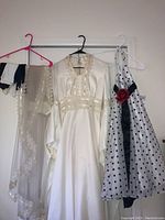 Wide shot showing ivory vintage wedding dress, ivory lace veil and white gloves on left side, girls' black and white polka dot formal dress hanging on right side