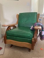 Full view of vintage rocking chair with green embossed Naugahyde horse head upholstery and solid wood frame with wagon wheel sides.