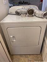 Front view of white Whirlpool electric dryer with flexible duct hose and vent attachments on top, showing appliance size and condition.