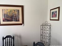 Photo showing the two framed prints on a white wall and the black metal wine rack to the right.