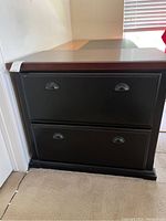Front view of the dark wood lateral file cabinet showing two drawers with metal cup handles and carpeted floor background