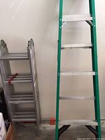 Photo showing folded silver ladder next to green ladder showing height difference.