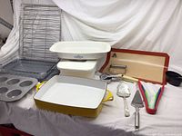 Overview of bakeware and utensils including yellow Dansk enamel cast iron pan, glass baking dishes, muffin tin, cooling racks, utensil holder, and various kitchen utensils.