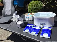 Massage seat cushion with wired remote, new water flosser, Salon Sundry paraffin wax therabath with packs of wax pellets on black table outdoors