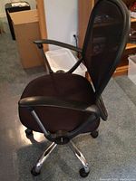 Side angle view showing padded seat, armrest, mesh backrest, and chrome wheeled base.