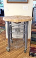 Front view of round butcher block rolling kitchen table showing metal legs, wire shelves, and wheels.