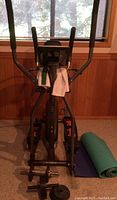 Front view of the exercise machine with weights at the base and yoga mats beside it.