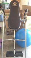 Body Power inversion table with padded backrest, foot rests, and silver frame. Blue exercise ball partially visible behind.