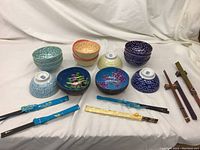 Full set of porcelain bowls in blue, red, purple patterns, two coconut shell bowls, six pairs of chopsticks arranged with holders, and hand-painted plate visible