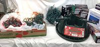 Photo showing multiple strands of Christmas lights, some lit, white packaging, and a green metal Christmas tree stand with a 'Canada's Advantage' label.