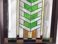 Close-up of lower left corner stained glass with green chevron pattern and amber, burgundy, black glass accents.