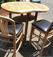 Photo of oval teak tall patio table with two matching tall chairs outside, showing overall condition and sun faded wood.