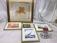 Photo showing three framed sailboat watercolor prints, a framed batik horse print, a small decorative tray, and a ceramic cup with saucer