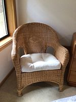 Woven wicker chair with diamond design on back, off white cushion on seat, photographed from front left angle.