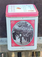 Side view showing a wartime procession black and white photo with decorative red accents on the tin.