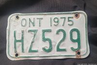 Front view of 1975 Ontario motorcycle license plate with green embossed numbers HZ529 on white background showing mounting holes and slight wear.