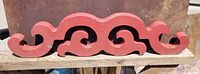 Photo of front view of red painted Gothic wooden architectural salvage piece showing scrolling cutout pattern and worn edges