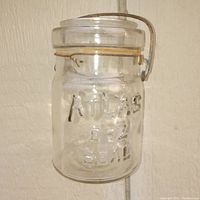 Front view of clear glass Atlas EZ Seal canning jar showing raised lettering and metal wire clasp, no lid present.