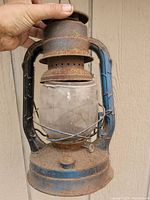 Front view of the antique blue metal lantern showing the rust on the base and broken glass globe.