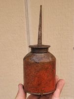 Front view of antique metal oiler bottle showing rusted reddish patina and narrow spout