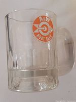Clear glass mini mug with A&W Rootbeer circular logo in orange and white on front, showing handle and embossed base.