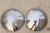 Two chrome Chevy wheel hub caps placed on a surface showing reflections and the Chevy bowtie emblem.