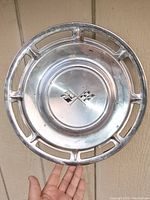 Front view of the vintage Chevy Corvette 15-inch hubcap showing the crossed flag emblem and the chrome finish with wear.