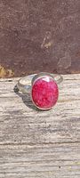 Front view of silver plated ring with natural red ruby oval cut stone set on top, resting on wooden surface.