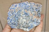 Photo of sodalite rock specimen held in hand showing blue, white, pink hues, and crystalline texture