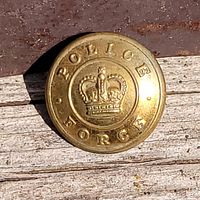 Close up photo of antique gold tone uniform button with crown emblem and 'POLICE FORCE' text on wood background.