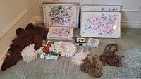 Full lot showing three placemat sets with floral designs, faux feather scarves, curtain tiebacks, lace doilies. Items arranged on carpet.