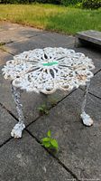 Side view of the white cast iron garden side table on a stone patio, showing three legs ending in claw feet and the intricate round top design.