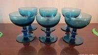 Six blue hand blown champagne glasses shown on a flat surface.