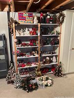 Wide shot showing multiple shelves filled with Christmas decorations including figurines, wreaths, ornaments, candles, and tabletop trees, plus additional items on the floor in front of the shelves.