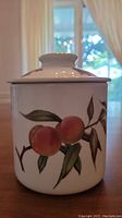 Front view of cookie jar showing peaches and leaves design on jar body with lid on.