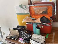 Multiple cosmetic bags, Samsonite orange cosmetic case open with compartments, various pairs and cases of glasses including a solar travel alarm.