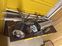 Photo showing GE A-C motor placed on a wooden surface with several metal rods, pipes and plates scattered around it.