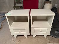 Front view of two white painted wood nightstands showing open shelf and drawer with ceramic knob