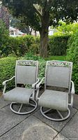 Two weathered swivel rocking patio chairs placed outdoors on paving stones in garden setting.