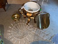 Wide view of metal plant pot holder, brass log holder, wire racks, and metal bowls arranged on floor.